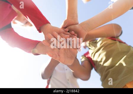 Directly below shot of multiracial elementary schoolboys stacking hands while standing against sky Stock Photo