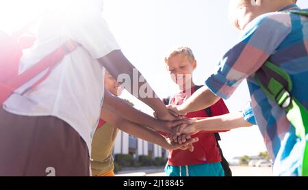 Happy multiracial schoolboys stacking hands while standing in school campus Stock Photo