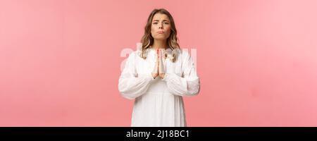 Portrait of hopeful clingy girlfriend, blond girl begging for favour in white dress over pink background, sobbing make cute eyes, pleading or praying Stock Photo