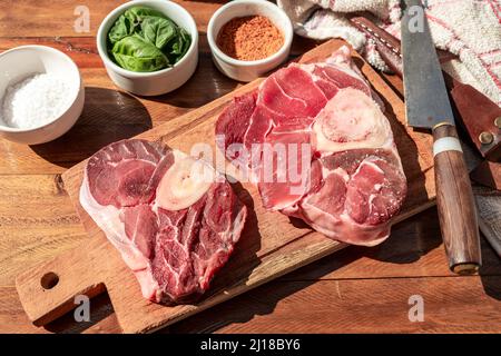 Two steaks of raw beef ossobuco on a wooden board with seasoning to flavour the pieces of meat. Animal protein concept, cheap cuts of beef. Aereal vie Stock Photo