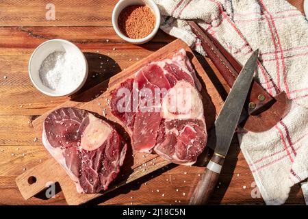 Two steaks of raw beef ossobuco on a wooden board with seasoning to flavour the pieces of meat. Animal protein concept, cheap cuts of beef. Aereal vie Stock Photo