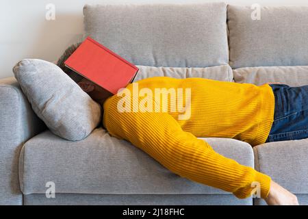 Man lying on the sofa sleeping with an open book covering his face. Relaxing at home concept Stock Photo