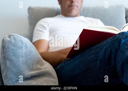 Unrecognizable man sitting in an armchair reading a book. Focus on the book Stock Photo