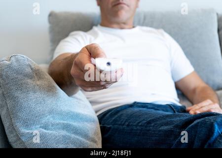 Unrecognized man pointing with tv's remote control from sofa with focus on the hand Stock Photo