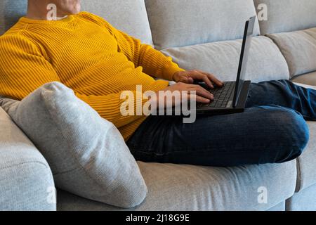 Man using a laptop sitting on the sofa. surfing the internet from home. Staying at home Stock Photo