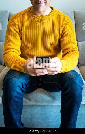 Close-up of smiling man using smartphone sitting on sofa. Connected from home Stock Photo