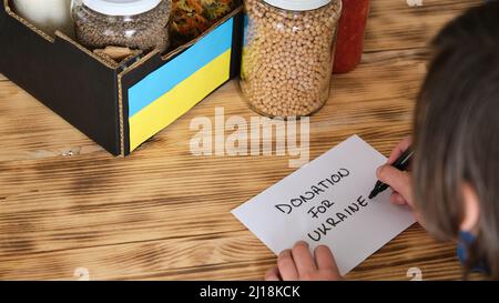 A Person preparing a box with food to donate to the war in Ukraine. Stock Photo