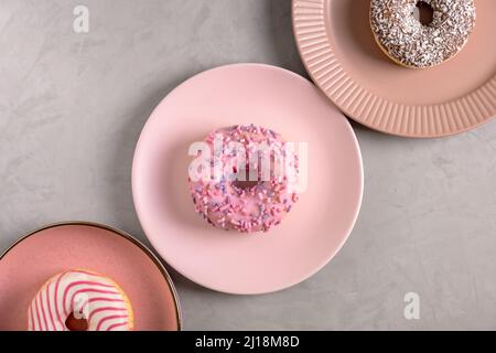 Three glazed donuts lie on tall pink plates Stock Photo