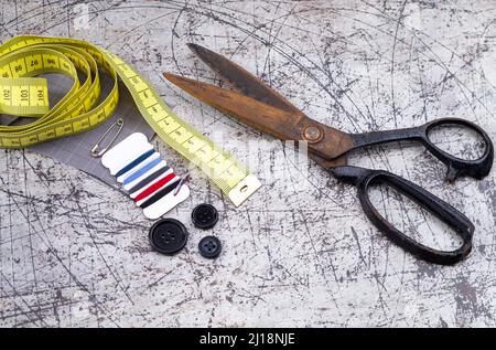 The photo shows an old rusty scissors on a gray background with various sewing utensils Stock Photo