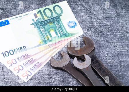 The photo shows various rusty wrenches on a gray background with euro banknotes Stock Photo