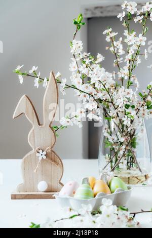 Wooden Easter bunny with blooming tree branch with flowers in the vase and colored easter eggs in container on the white table. Happy Easter spring ve Stock Photo