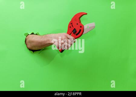 A man holds a tool for cutting plastic pipes on a green background Stock Photo