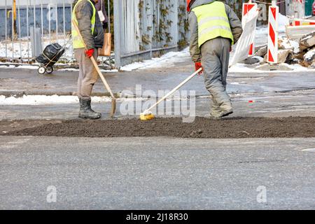 Road workers using a shovel and brush patch up the road surface on the roadway and cover it with fine gravel. Copy space. Stock Photo