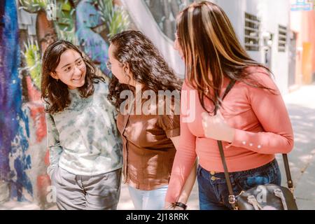 Three young women are walking down the street, they are smiling, playing and having a good time. Stock Photo