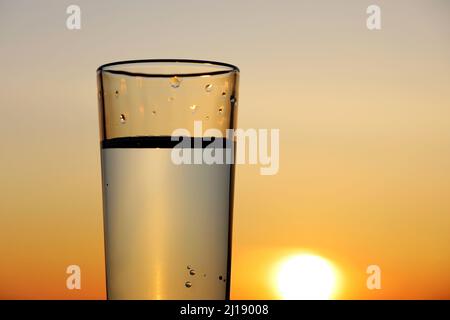 Clean water in drinking glass on sunset sky background. Water purification, freshness and thirst Stock Photo