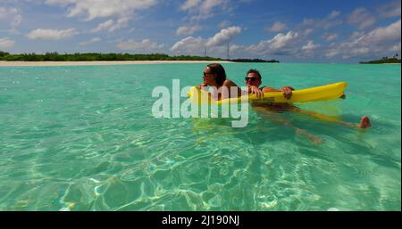 A view of man holding woman on yellow inflatable mattress in water Stock Photo