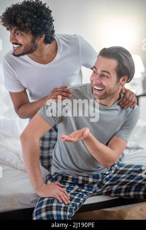 Cheerful biracial gay couple sitting in the bedroom Stock Photo