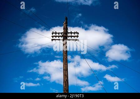 Telegraph pole against a blue sky with white clouds, telephone wires going off in all directions. Stock Photo