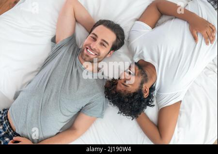 Romantic biracial gay couple resting in bed Stock Photo