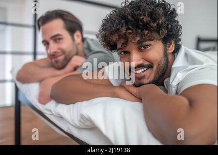 Young biracial gay couple lying in bed Stock Photo