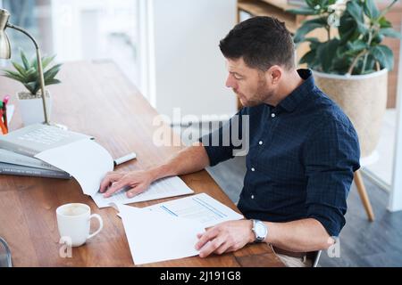 Carefully reading through an important section in the document. Shot of a handsome mature businessman looking through some paperwork while sitting in Stock Photo