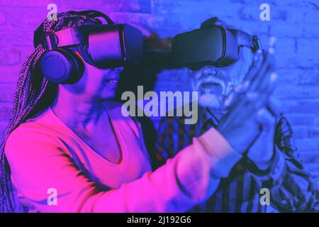 Multiracial senior friends having fun dancing while using virtual reality goggles - Focus on left headset Stock Photo