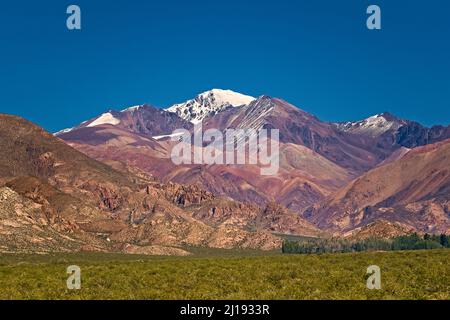 Snowy peak behind multicolored mountains in natural reserve El Leoncito, in the province of San Juan, Argentina. Stock Photo