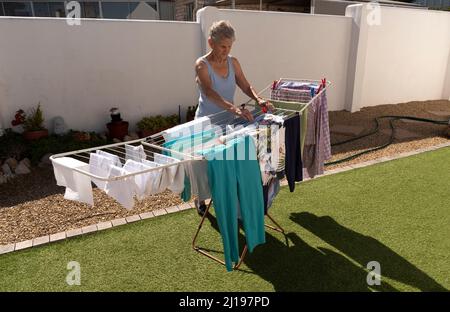South Africa. 2022. Elderly woman hanging washing out to dry in the garden on a sunny day. Stock Photo