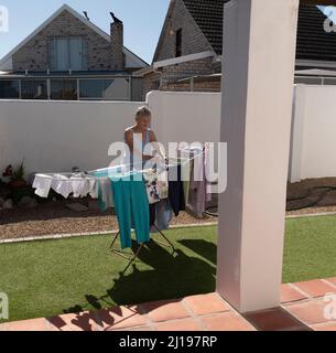 South Africa. 2022. Elderly woman hanging washing out to dry in the garden on a sunny day. Stock Photo