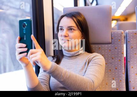 Interested female traveler filming landscapes behind glass in express train Stock Photo