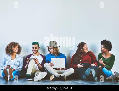 The most tech savvy generation there is. Studio shot of a group of young people sitting on the floor and using wireless technology. Stock Photo