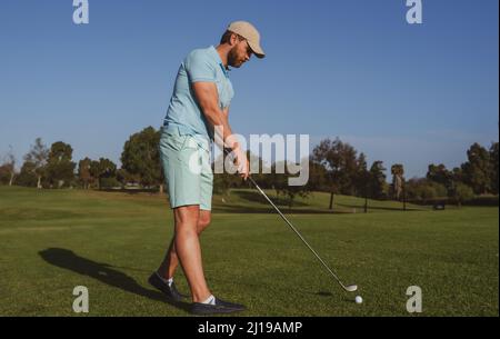 Golf player playing golf on sunny day. Professional golfer taking shot on golf course. Stock Photo