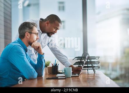 Let me take a look.... Shot of two businessmen working on a laptop in their office. Stock Photo