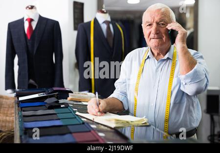 Professional tailor man talking on mobile phone and making notes in notebook Stock Photo