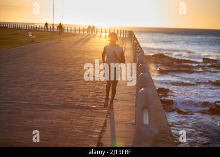 Running along her favorite route at sunset. A young woman running along the promenade at sunset. Stock Photo