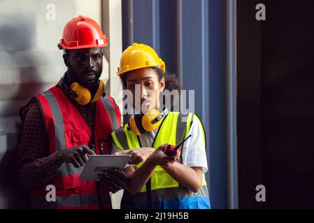 Two African american male and female worker using tablet and checking control loading freight containers from Cargo freight ship for import export. Stock Photo