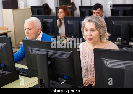 Young and mature men and women coworkers sitting, working on computers Stock Photo