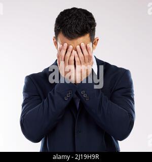 Somebody save me from this misery. Studio shot of a young businessman covering his face against a white background. Stock Photo