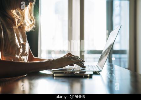 Crop photo of  blonde woman with long hair working on laptop and using mobile phone at home, remote work Stock Photo