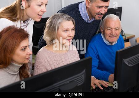 Elderly people working on computer with young teacher Stock Photo