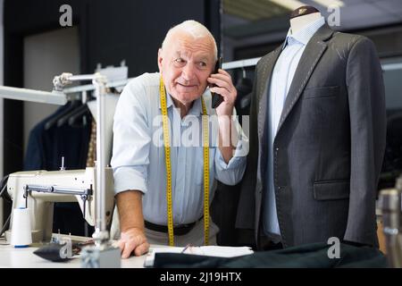 Professional tailor communicates with the client on mobile phone and takes notes in notebook Stock Photo