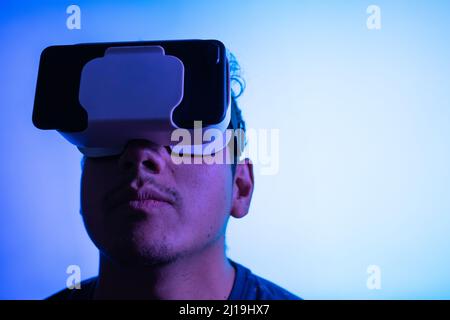 Young latin man using Virtual Reality VR Headset 3D Glasses. Studio blue screen backdrop. Low key.  Stock Photo
