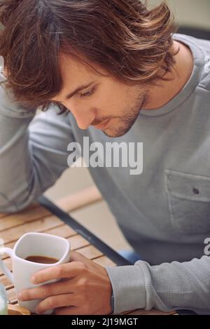 Thinking about the day ahead. Shot of a young man looking thoughtful while drinking a coffee. Stock Photo