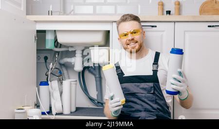 Plumber working install new cartridge for cold water filter in white kitchen. Stock Photo