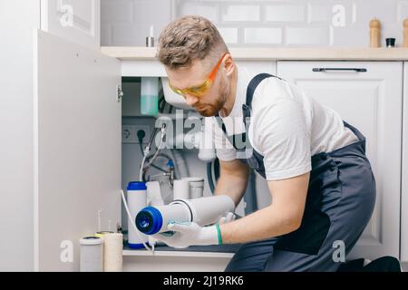 Plumber working install new cartridge for cold water filter in white kitchen. Stock Photo