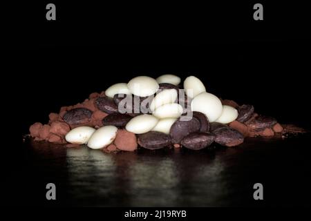 Dark and white couverture chocolate drops lying on cocoa powder, studio photography with black background Stock Photo