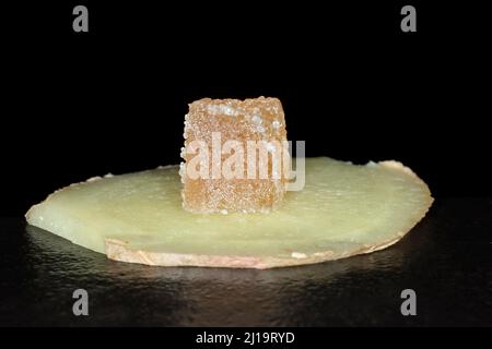 Candied ginger cut into cubes lies on a slice of fresh ginger, studio photography with black background Stock Photo