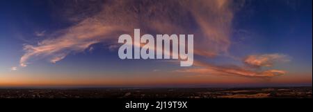 Fluffy pink clouds at sunset against a deep blue sky aerial panoramic Stock Photo