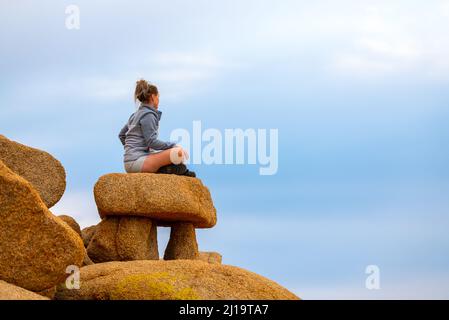 Woman tourist seen in Joshua Tree National Park waiting for sunset views over the desert landscape. Stock Photo