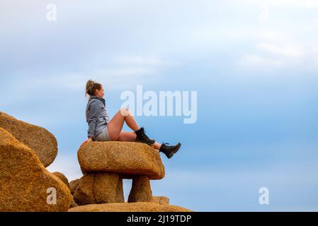 Woman tourist seen in Joshua Tree National Park waiting for sunset views over the desert landscape. Stock Photo